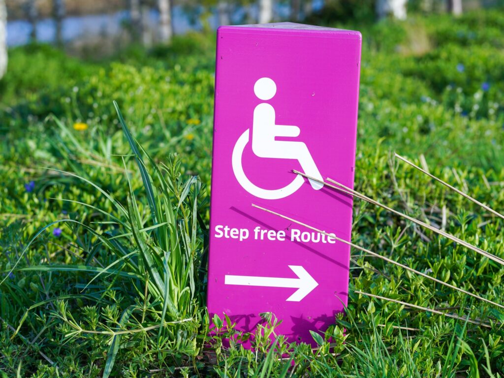 A stock image representing the accessibility them. The photo shows a sign with a wheelchair icon and "Step free Route" written under it. The sign is placed on grass