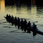 An image of a rowing team’s silhouettes against the water.